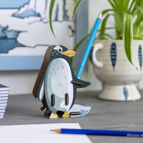 Pinguin Kuno hält einen Stift griffbereit auf dem Schreibtisch