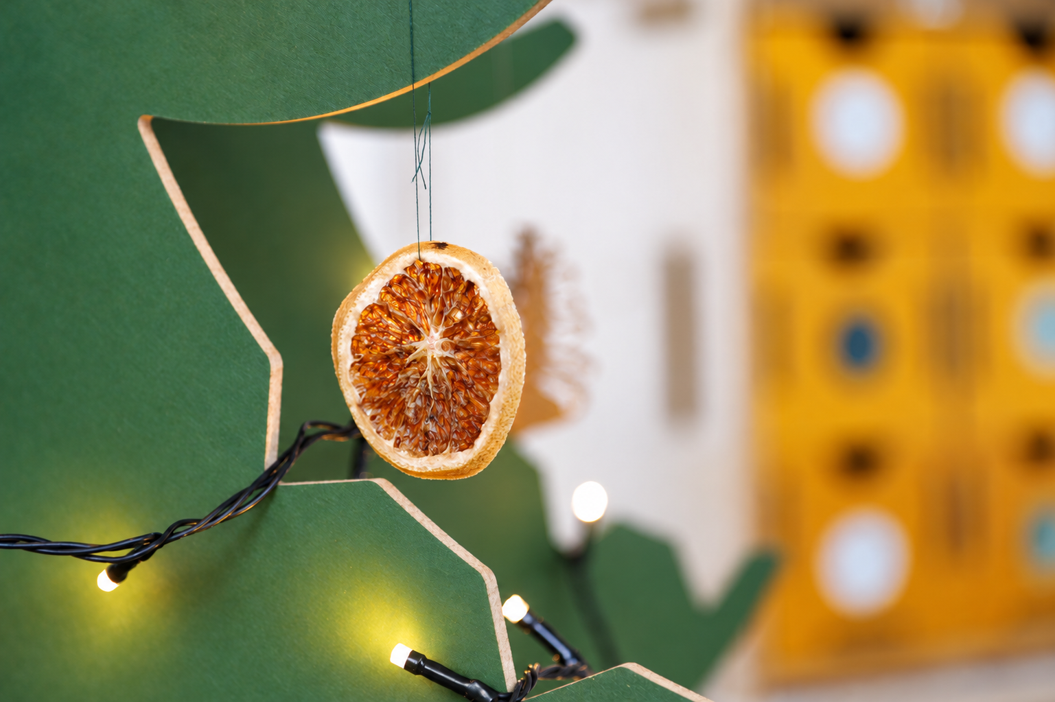 Detail eines gr&uuml;nen MDF-Weihnachtsbaums mit getrockneter Orangenscheibe als Anh&auml;nger und leuchtender Lichterkette